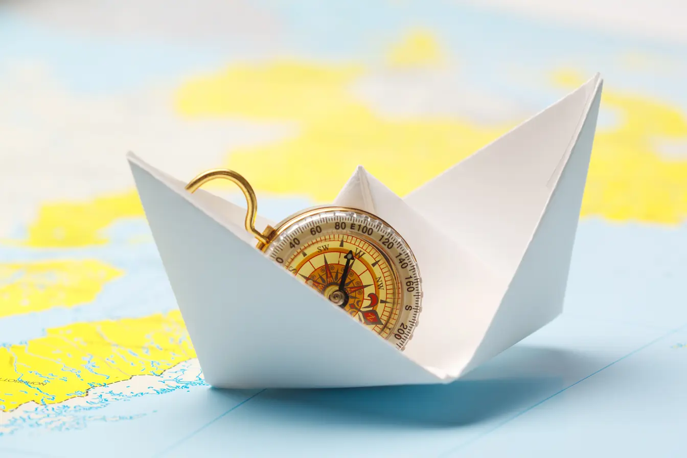 Assurance voyage multirisque Bateau en papier et boussole sur une carte – choisir son assurance voyage